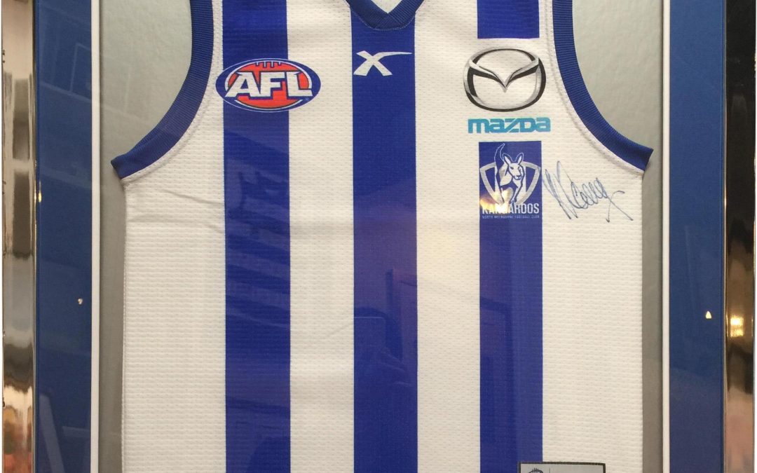 North Melbourne football jumper signed by Wayne Carey framed in a modern gun metal metallic frame with blue and white double mat boards.