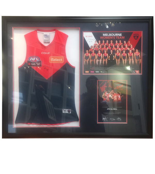 A Melbourne womens football club jersey, team photo and certificate of authenticity framed in black frame with double mat board surround and UV glass.