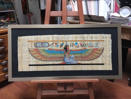 A large Egyptian papyrus floated on a black mat board surround framed in a silver/gold frame.