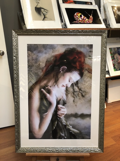 A print of a woman framed in a silver ornate frame with a mat board surround and glass.