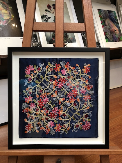 A floral tapestry floated on a white mat board with a spacer and glass framed in a black timber box frame.