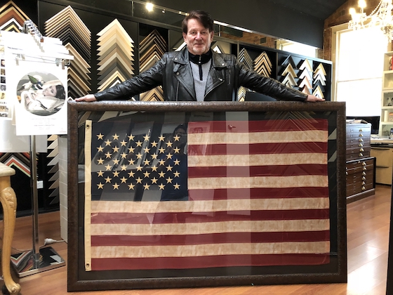 Greg Mahoney with a large American flag floated and framed in a wide dark walnut frame with an acrylic front.