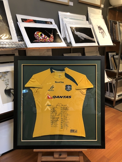 A Wallabies jersey framed in a wide black box timber frame with double mat boards and glass.