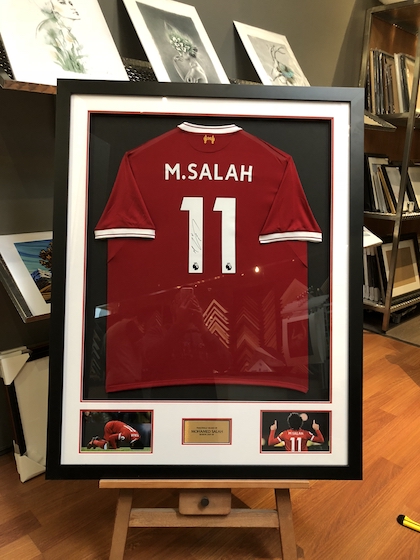 A hand signed Liverpool jersey framed in a black box frame with 2 mat boards, printed photos, plaque and glass.