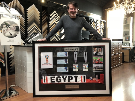 Greg Mahoney with a collection of memorabilia from the 2018 World Cup framed in a large black box timber frame with multiple opening mat board surround, silver plaque and acrylic front.