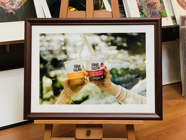 A Like Licks company promotional photograph framed in a walnut timber frame with white mat board surround and glass.