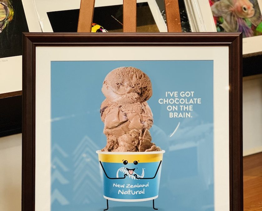 A promotional poster for New Zealand natural icecream company that has been framed in a walnut frame with a mat board surround and glass.