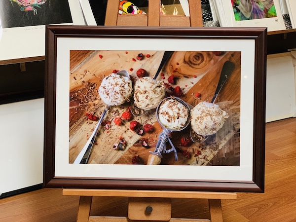 A New Zealand natural icecream company promotional poster framed in a walnut frame with a white mat board surround and glass.