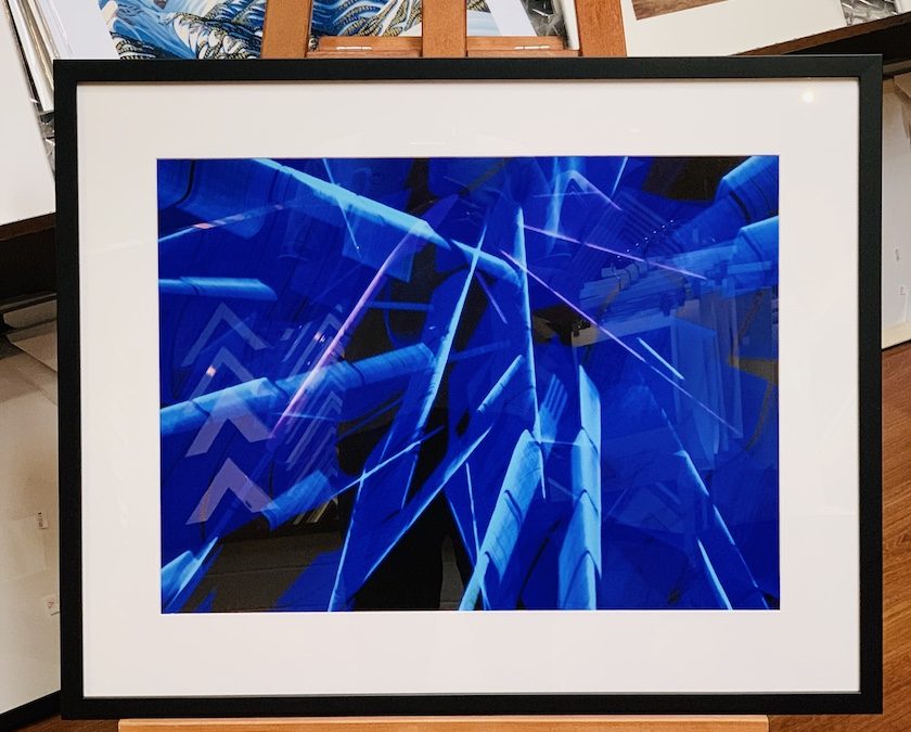 An abstract light photograph framed in a black timber frame with a white mat board surround and glass.