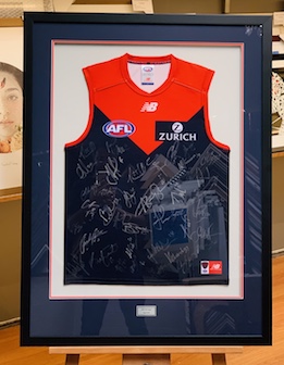 This is a signed Melbourne jersey with a raised double mat surround and the jersey floated on a soft grey mat board. The frame is black and we have added a plaque at the bottom of the frame. We have opted for UV glass to prevent the signatures from fading