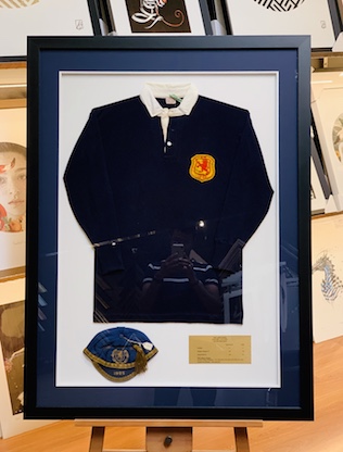 A Scottish national soccer jersey and cap that is nearly 100 years old. We framed the jersey, cap and plaque in a heavy black frame with a double mat surround a UV glass to protect the jersey