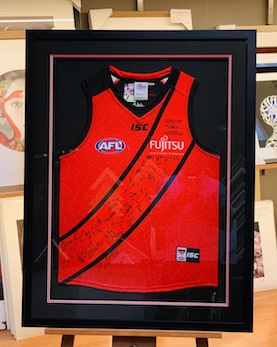 A footy jumper signed by the team in a black frame, double mat surround, mat backing and we have used UV glass to prevent the signatures from fading