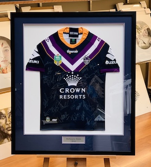 A Melbourne Storm signed by the whole team jersey with a double mat surround that picks up the colours of the Storm’s jersey with a white mat backing. We have then supplied the plaque and added a black frame with UV glass which prevents the signatures from fading